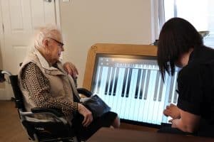 A resident and team member playing a virtual piano on a giant interactive tablet at Great Horkesley Manor Care Home near Colchester.