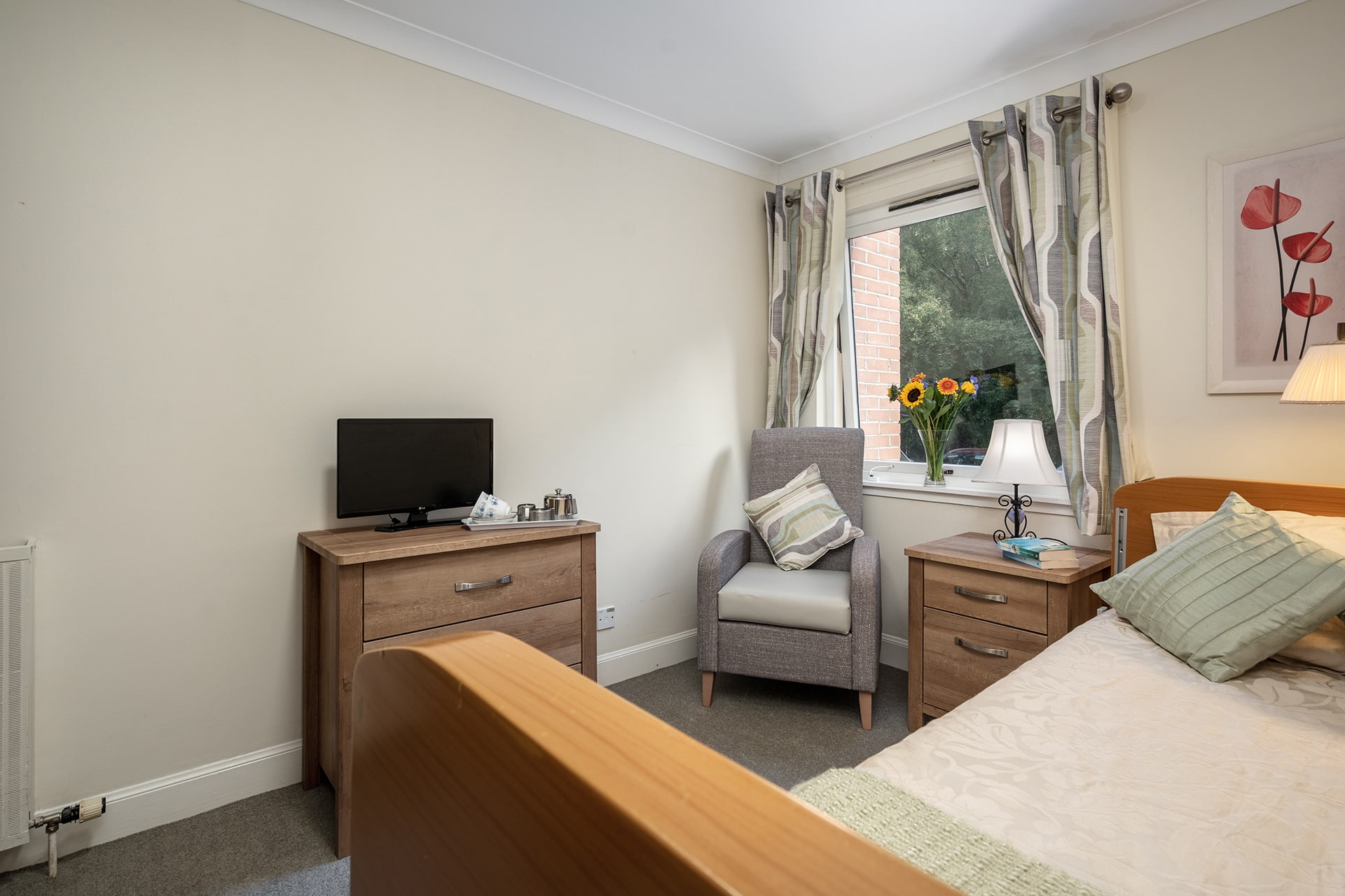 A cosy bedroom at Muirton House Care Home with a garden view.