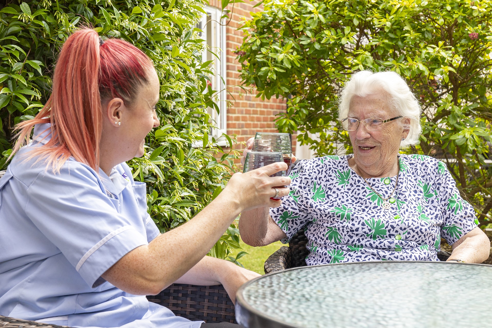 A resident and carer enjoy a cold drink on the garden terrace at Lily House Care Home in Ely.