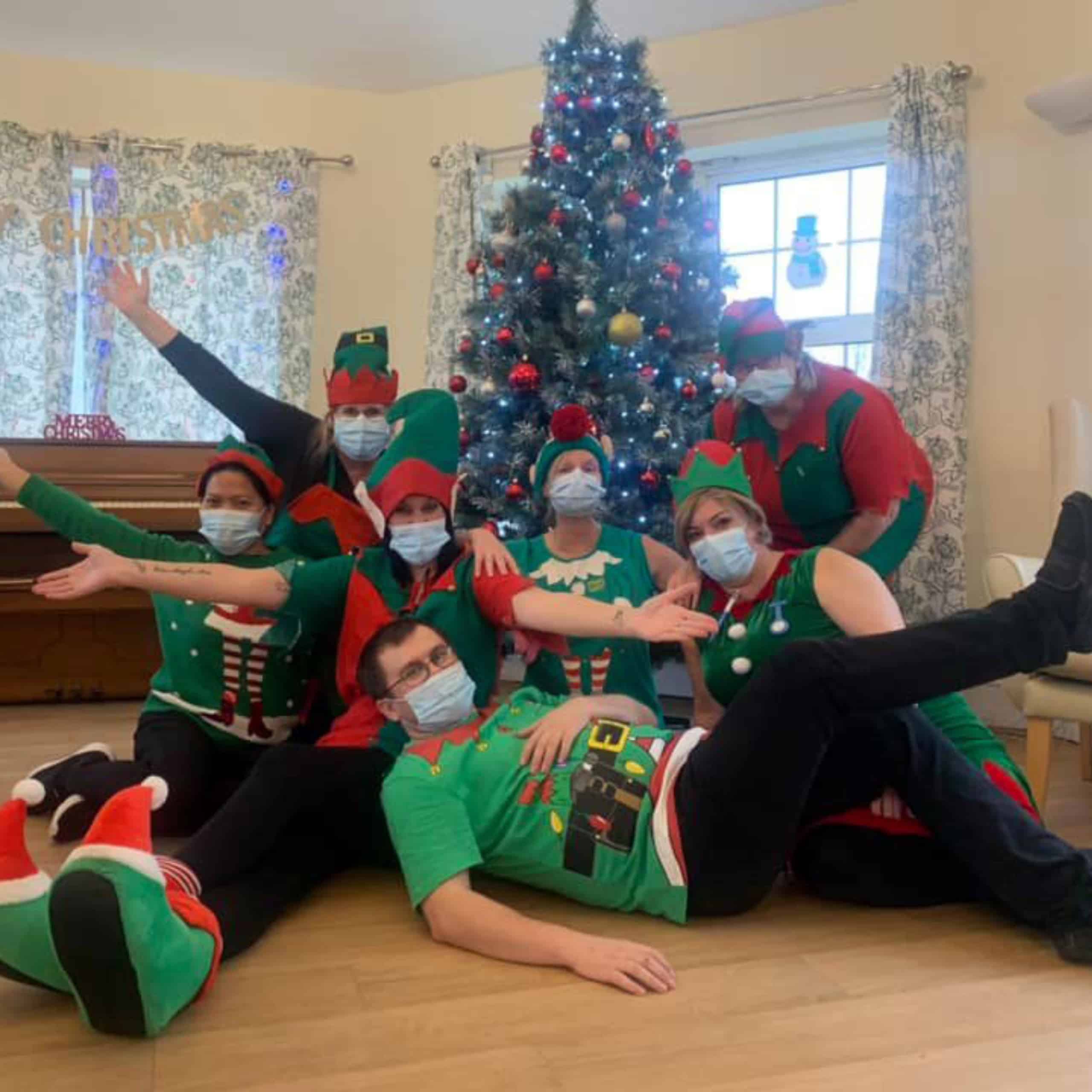 The Great Horkesley Manor Care Home team dressed in elf outfits, hats and fluffy elf boots in front of the home's beautiful Christmas tree.
